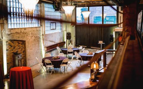 Round guest tables set for a reception beneath exposed brick and steel beams